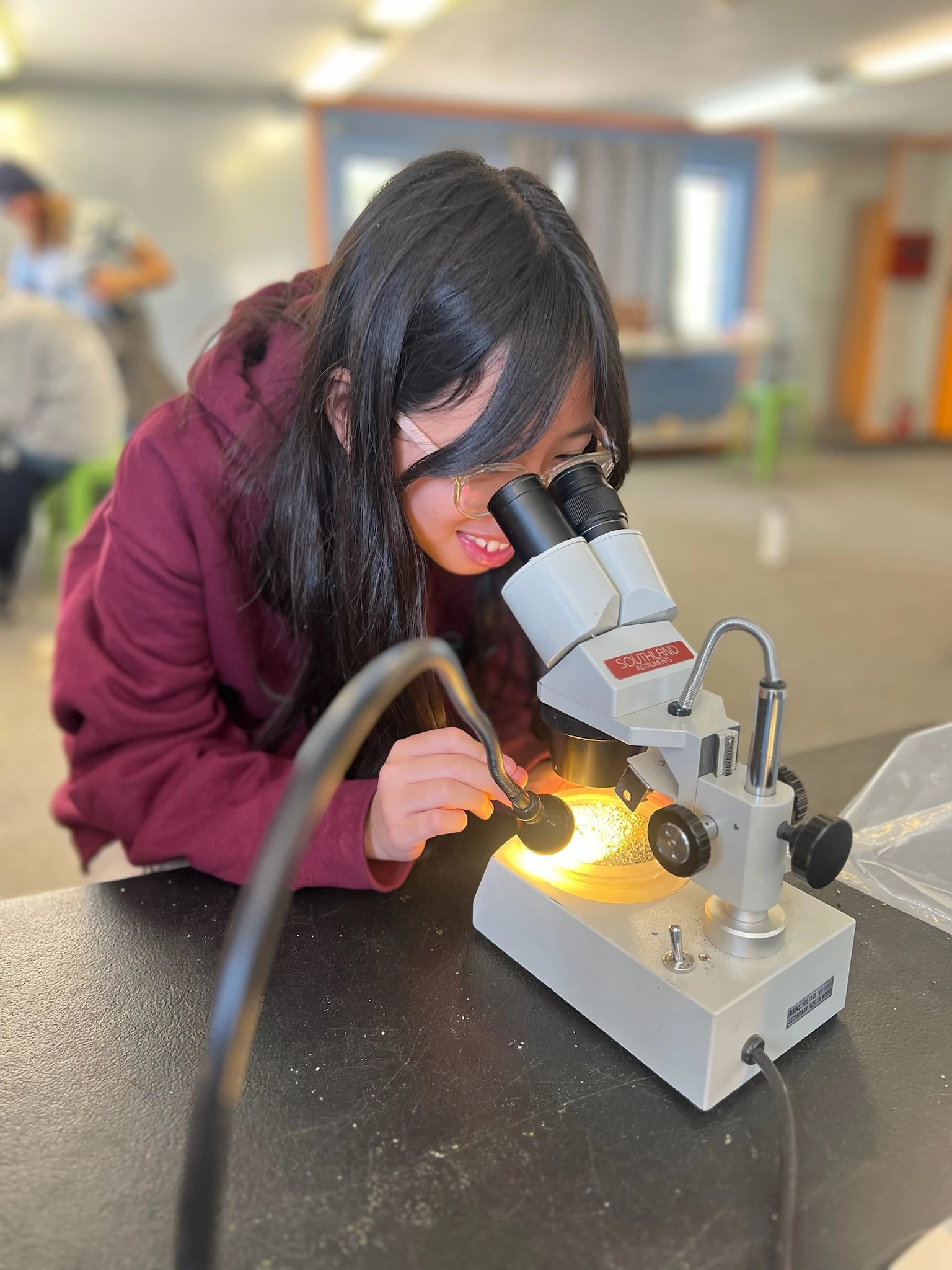 Page Academy student in an AstroCamp hoodie focusing a microscope on a lit sample
